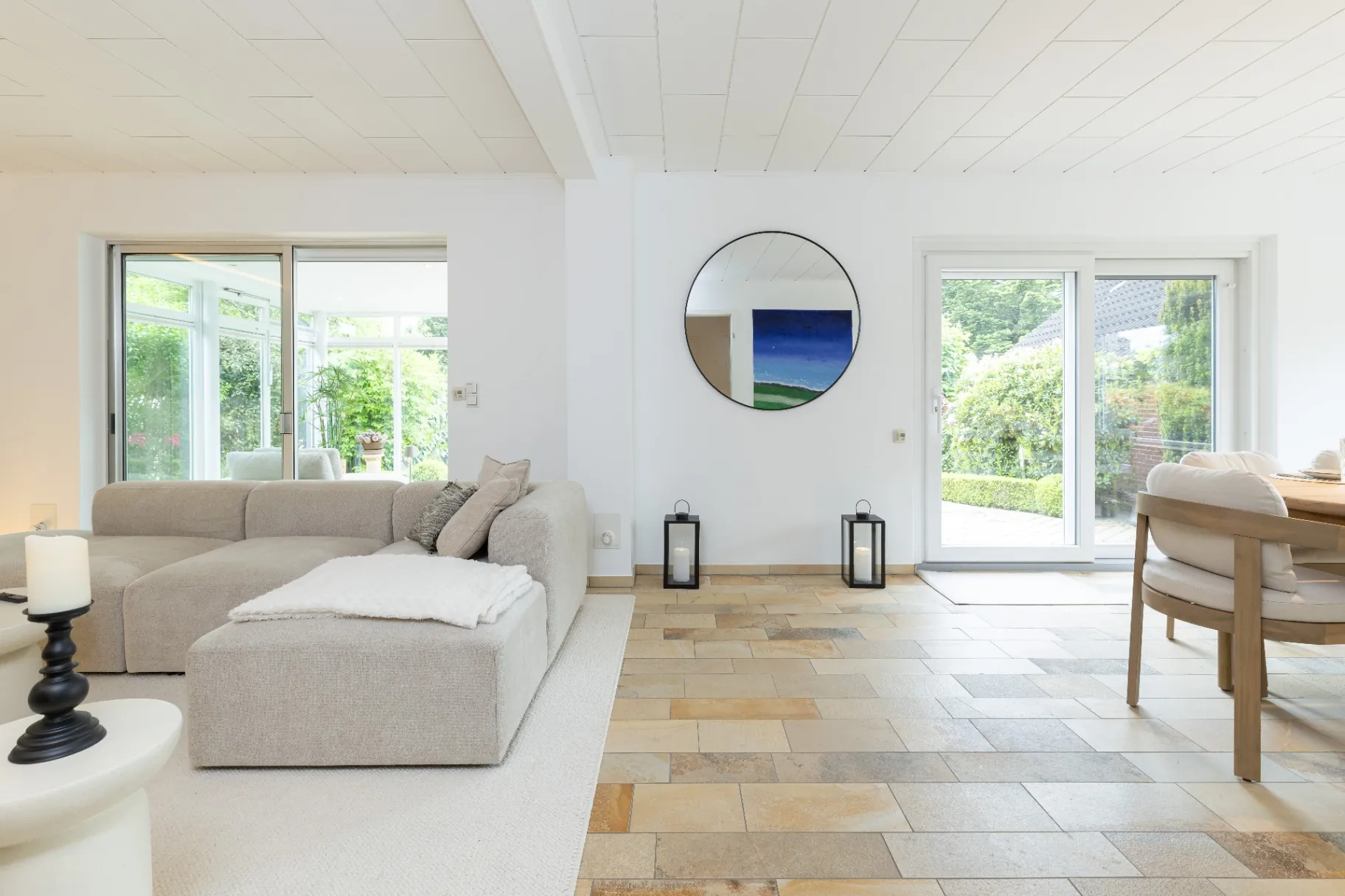 Heller Wohnbereich mit großem Sofa, Rundspiegel und Natursteinboden im Ferienhaus Smukke in Hattstedt